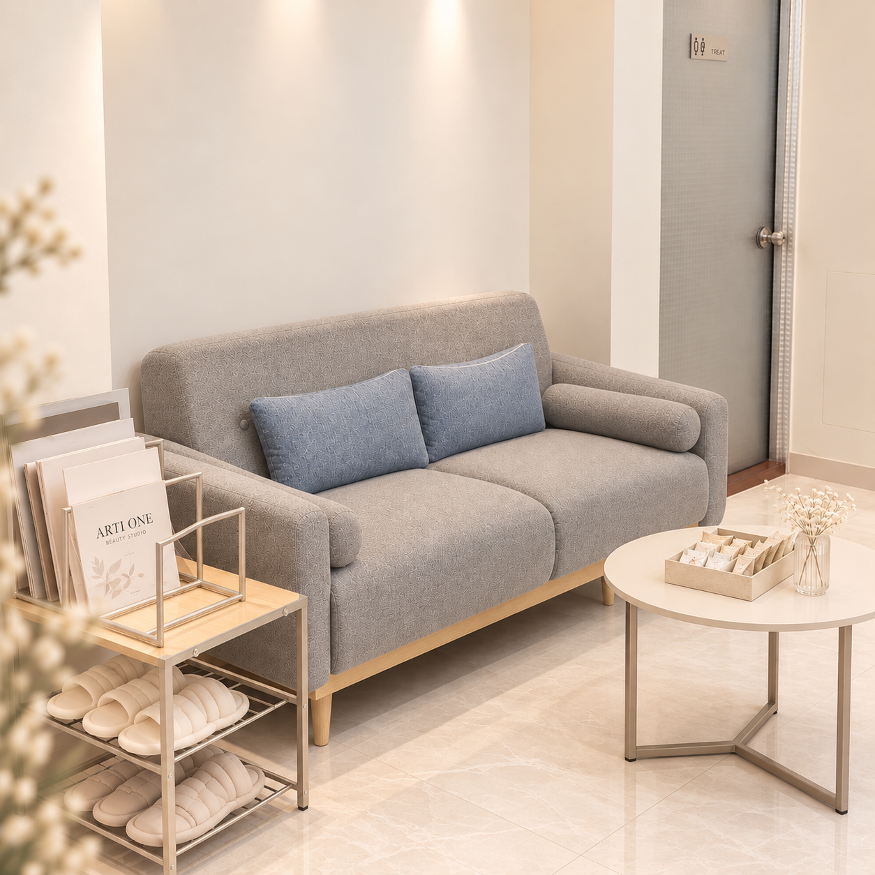 Studio waiting lounge with a grey sofa, cushions and a side table with magazines